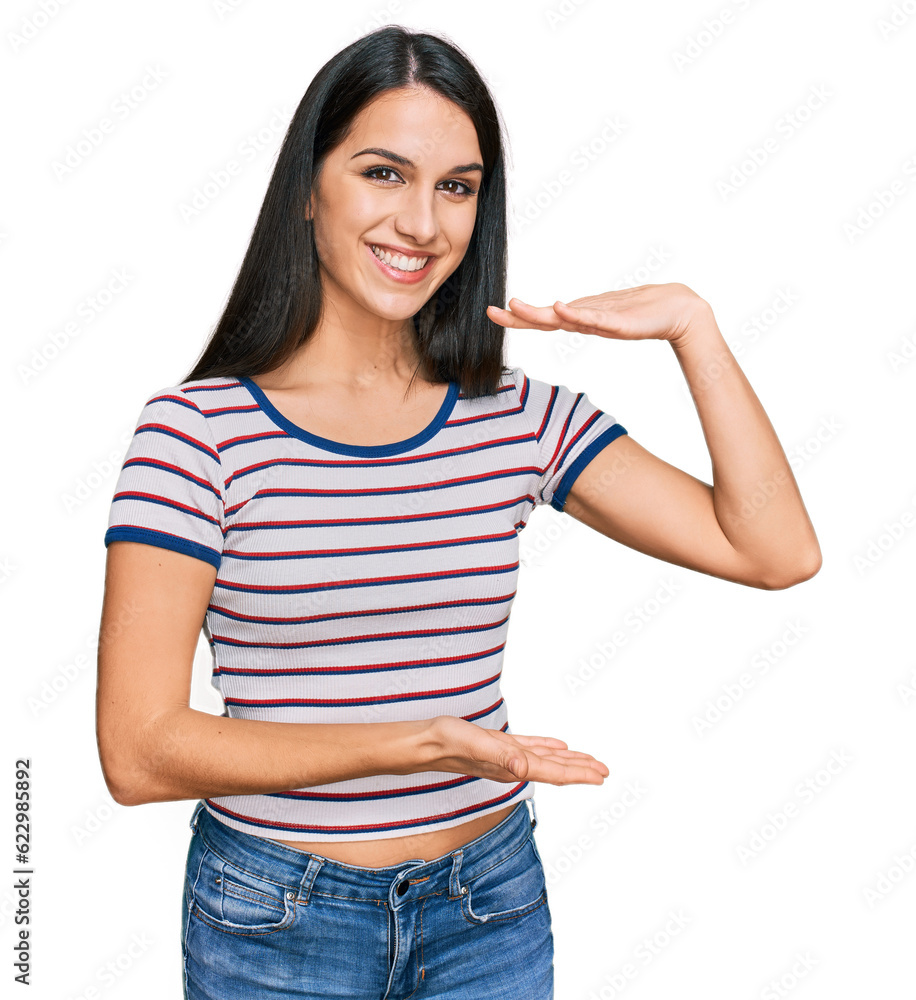 Young hispanic girl wearing casual striped t shirt gesturing with hands showing big and large size sign, measure symbol. smiling looking at the camera. measuring concept.