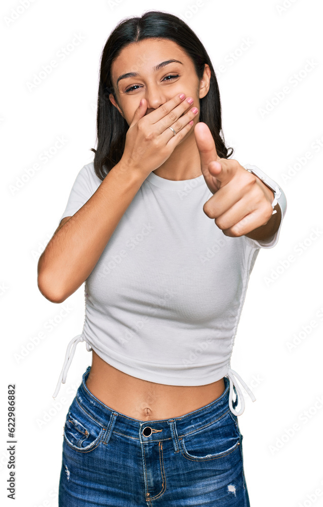 Young hispanic girl wearing casual white t shirt laughing at you, pointing finger to the camera with hand over mouth, shame expression Young hispanic girl wearing casual white t shirt laughing at you, pointing finger to the camera with hand over mouth, shame expression