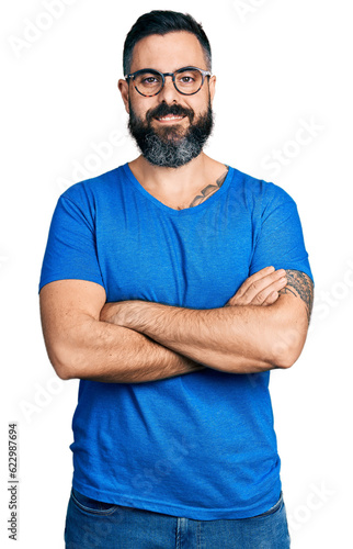 Hispanic man with beard wearing casual t shirt and glasses happy face smiling with crossed arms looking at the camera. positive person.