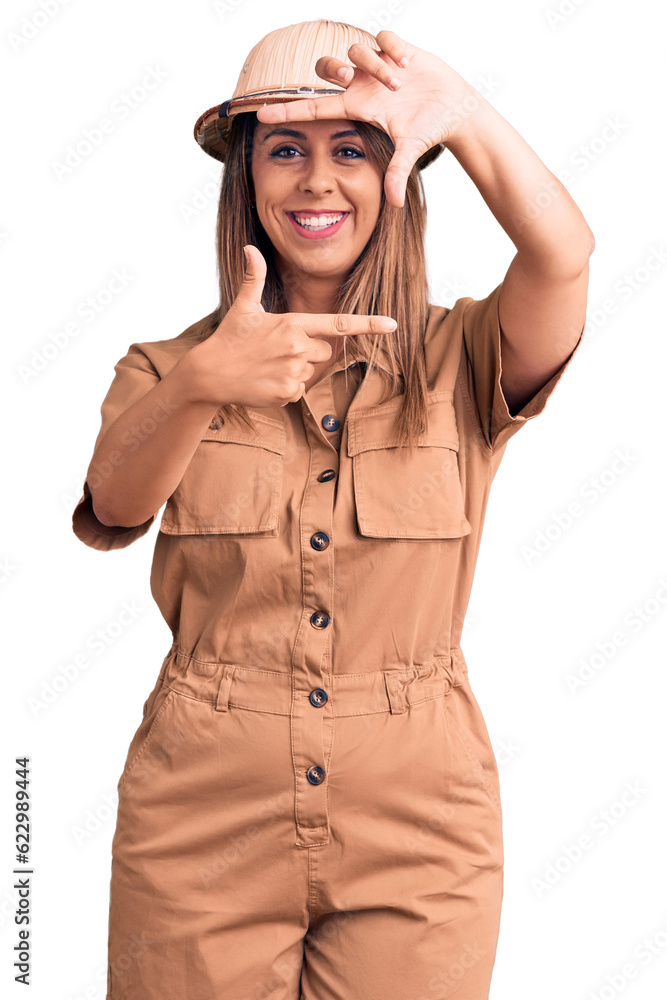Fototapeta premium Young beautiful woman wearing explorer hat smiling making frame with hands and fingers with happy face. creativity and photography concept.