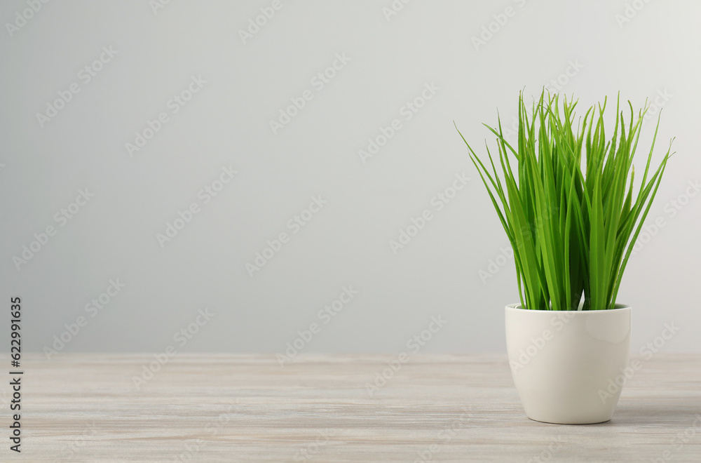 Beautiful artificial plant in flower pot on wooden table against light grey background, space for text Beautiful artificial plant in flower pot on wooden table against light grey background, space for text