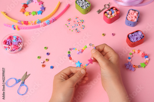 Bilde på lerret Child making beaded jewelry and different supplies on pink background, above view