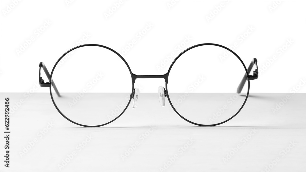 Fototapeta premium Round glasses with metal frame on table against white background