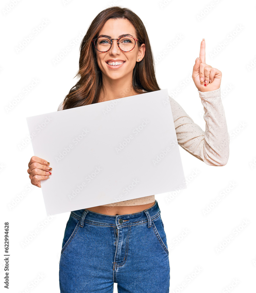 Young brunette woman holding blank empty banner surprised with an idea or question pointing finger with happy face, number one Young brunette woman holding blank empty banner surprised with an idea or question pointing finger with happy face, number one