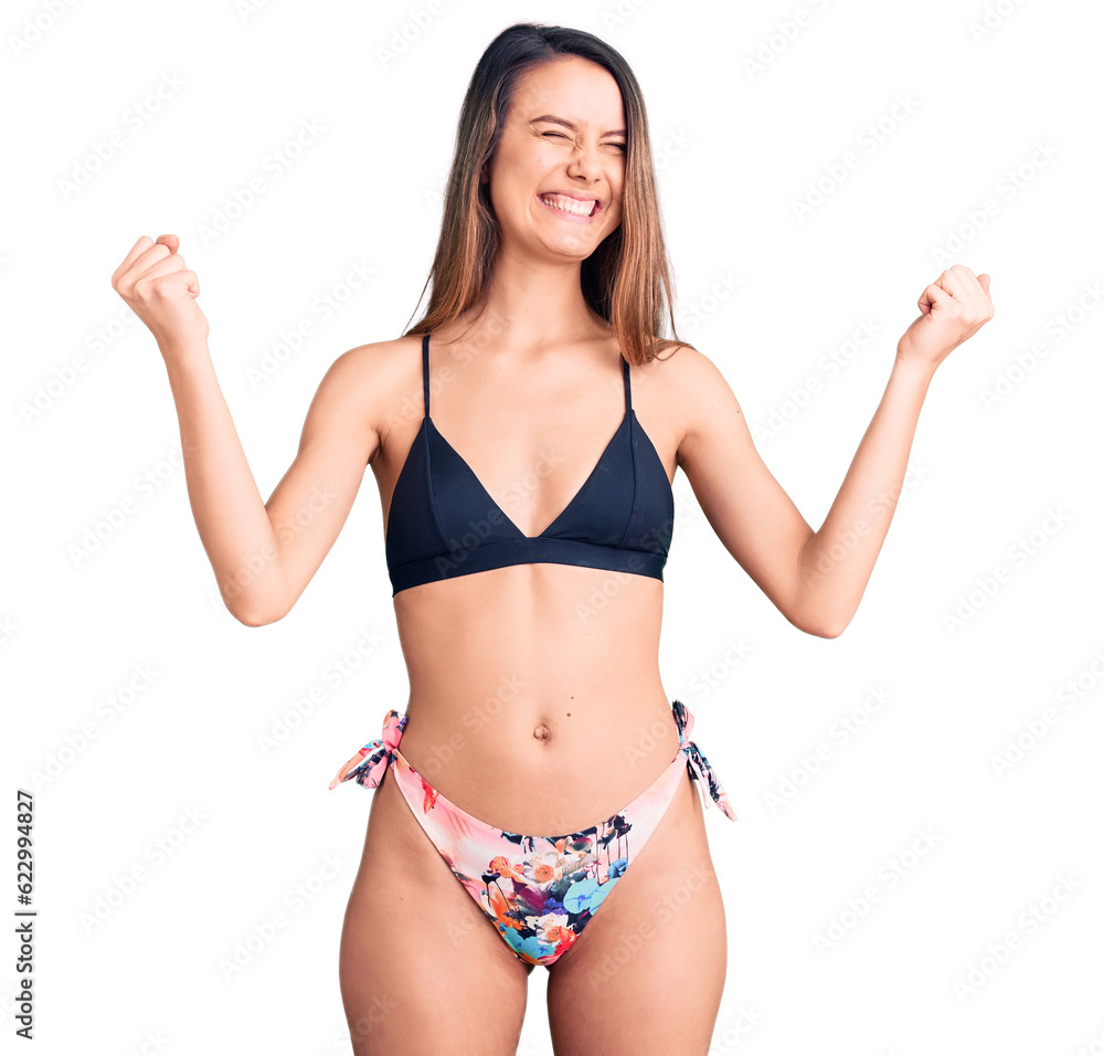 Young beautiful girl wearing bikini very happy and excited doing winner gesture with arms raised, smiling and screaming for success. celebration concept. Young beautiful girl wearing bikini very happy and excited doing winner gesture with arms raised, smiling and screaming for success. celebration concept.