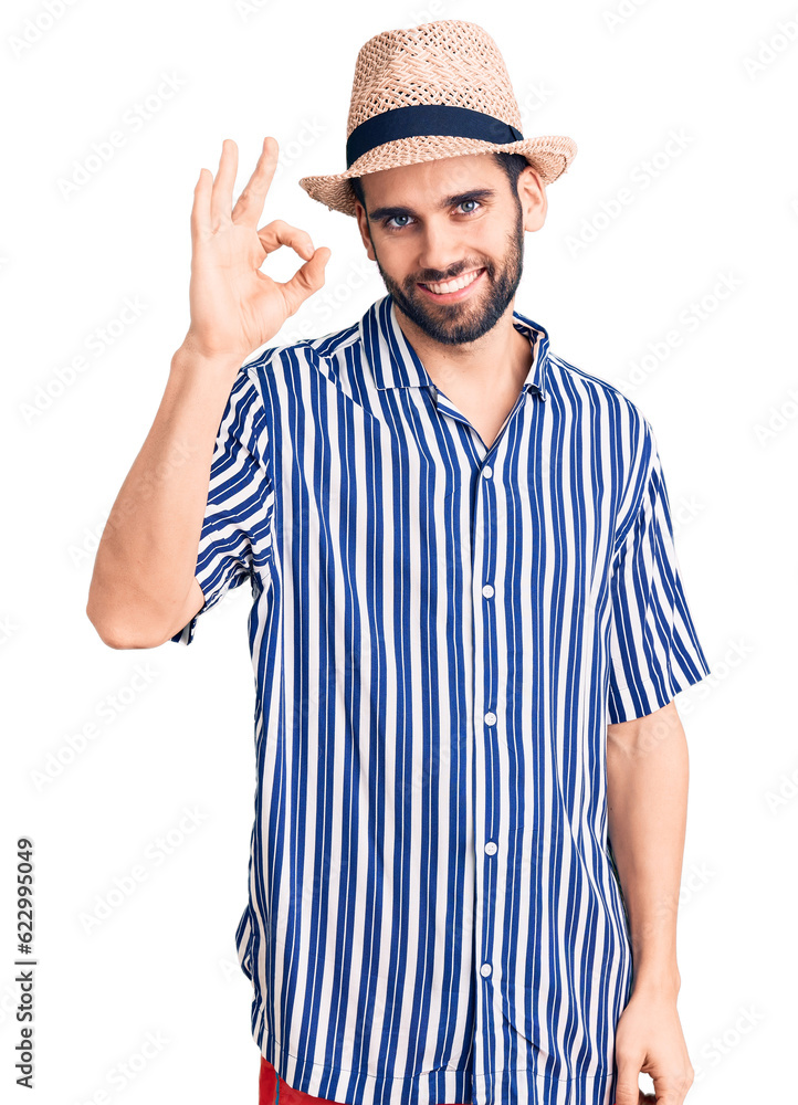 Young handsome man with beard wearing summer hat and striped shirt smiling positive doing ok sign with hand and fingers. successful expression. Young handsome man with beard wearing summer hat and striped shirt smiling positive doing ok sign with hand and fingers. successful expression.