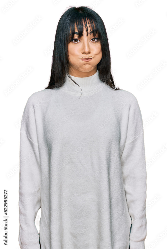 Young brunette woman with bangs wearing casual turtleneck sweater puffing cheeks with funny face. mouth inflated with air, crazy expression. Young brunette woman with bangs wearing casual turtleneck sweater puffing cheeks with funny face. mouth inflated with air, crazy expression.
