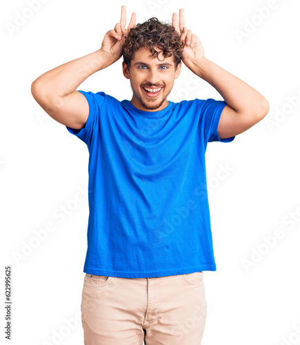 Young handsome man with curly hair wearing casual clothes posing funny and crazy with fingers on head as bunny ears, smiling cheerful