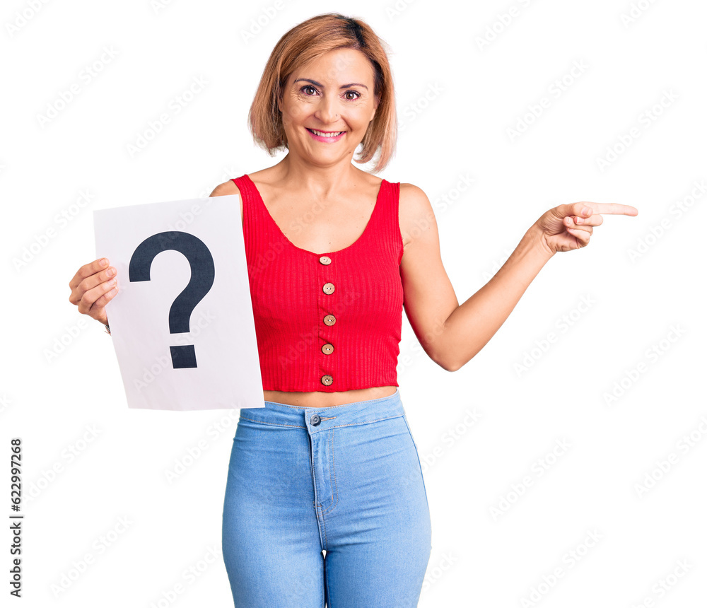 Young blonde woman holding question mark smiling happy pointing with hand and finger to the side Young blonde woman holding question mark smiling happy pointing with hand and finger to the side