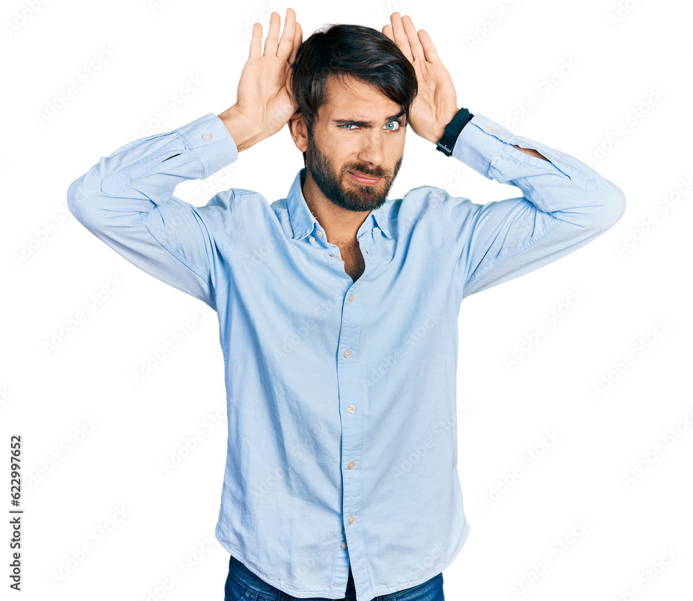 Hispanic man with blue eyes wearing business shirt doing bunny ears gesture with hands palms looking cynical and skeptical. easter rabbit concept. Hispanic man with blue eyes wearing business shirt doing bunny ears gesture with hands palms looking cynical and skeptical. easter rabbit concept.