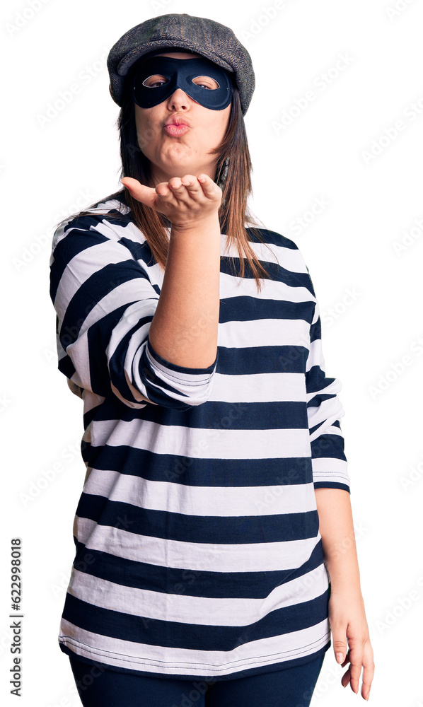 Young beautiful brunette woman wearing burglar mask looking at the camera blowing a kiss with hand on air being lovely and sexy. love expression. Young beautiful brunette woman wearing burglar mask looking at the camera blowing a kiss with hand on air being lovely and sexy. love expression.