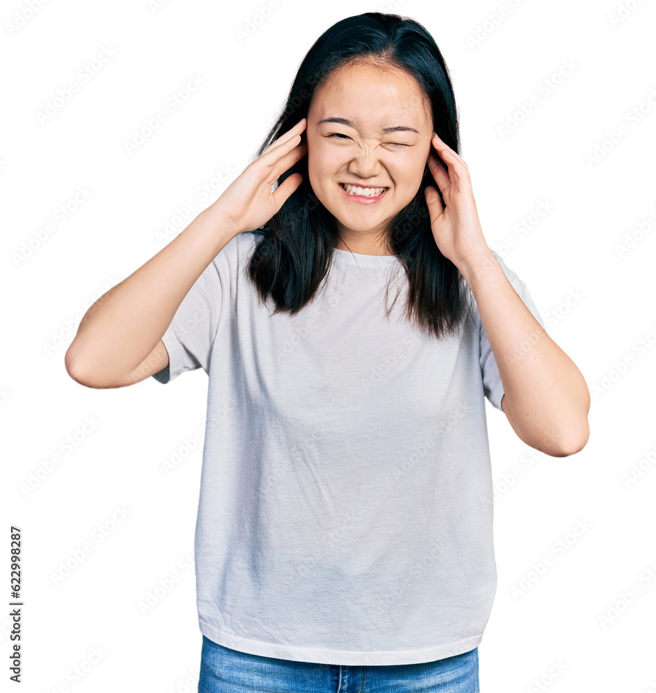 Young chinese woman wearing casual white t shirt covering ears with fingers with annoyed expression for the noise of loud music. deaf concept. Young chinese woman wearing casual white t shirt covering ears with fingers with annoyed expression for the noise of loud music. deaf concept.