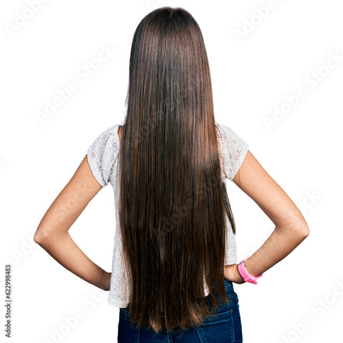Young brunette girl with long hair wearing white shirt standing backwards looking away with arms on body