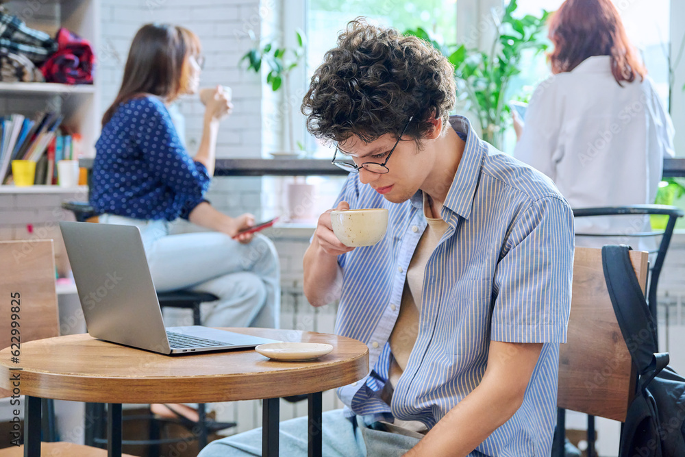 Guy college student with laptop sitting at table at coffee shop drinking cup of coffee Guy college student with laptop sitting at table at coffee shop drinking cup of coffee