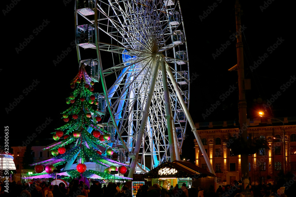 Carousel, Ferris wheel, Christmas tree. Fair on the city evening square