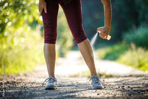 Woman applying insect repellent against mosquito and tick on her leg before running outdoors