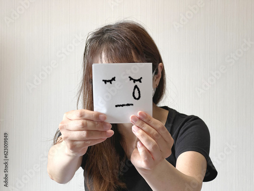 Photographie 顔の前で涙を流す顔イラスト入り紙を両手で持つ女性