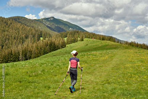 Young woman with sticks walking in the meadow and enjoying a beautiful view. Travel concept.