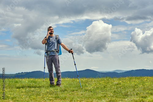 Handsome man standing in the meadow and making a call. Mountains on the background. Activity and technology concept.