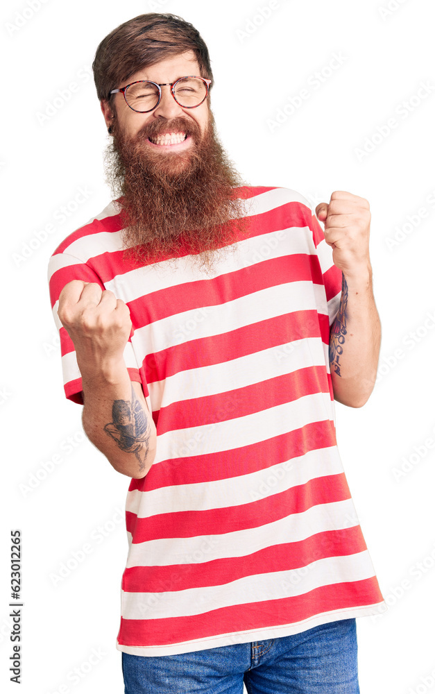 Handsome young red head man with long beard wearing casual clothes very happy and excited doing winner gesture with arms raised, smiling and screaming for success. celebration concept. Handsome young red head man with long beard wearing casual clothes very happy and excited doing winner gesture with arms raised, smiling and screaming for success. celebration concept.