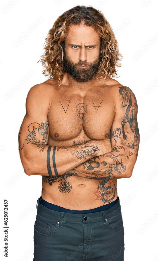 Fototapeta premium Handsome man with beard and long hair standing shirtless showing tattoos skeptic and nervous, disapproving expression on face with crossed arms. negative person.
