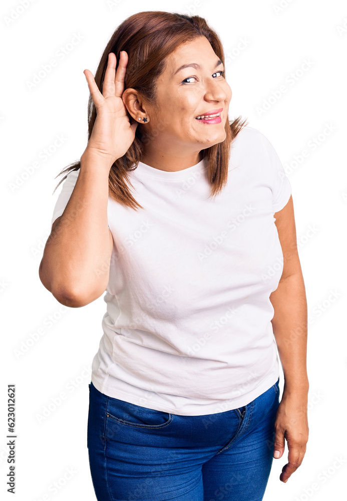 Middle age latin woman wearing casual white tshirt smiling with hand over ear listening an hearing to rumor or gossip. deafness concept. Middle age latin woman wearing casual white tshirt smiling with hand over ear listening an hearing to rumor or gossip. deafness concept.