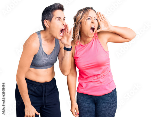 Couple of women wearing sportswear shouting and screaming loud to side with hand on mouth. communication concept.