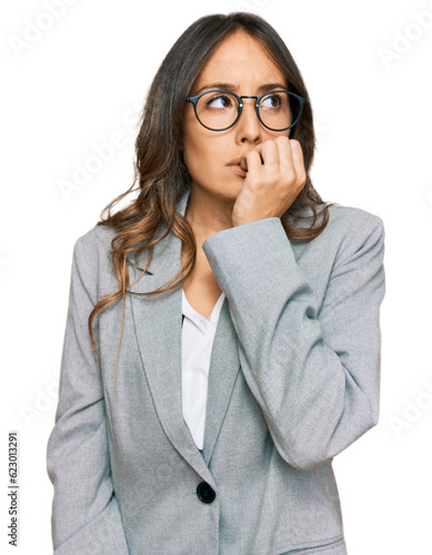 Leinwand Poster Young brunette woman wearing business clothes looking stressed and nervous with hands on mouth biting nails