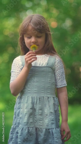 Beautiful cute little girl enjoy looking yellow dandelion and giving it in summer park. Sweet child with spring flower of blowball in midday light. Slow motion. Vertical