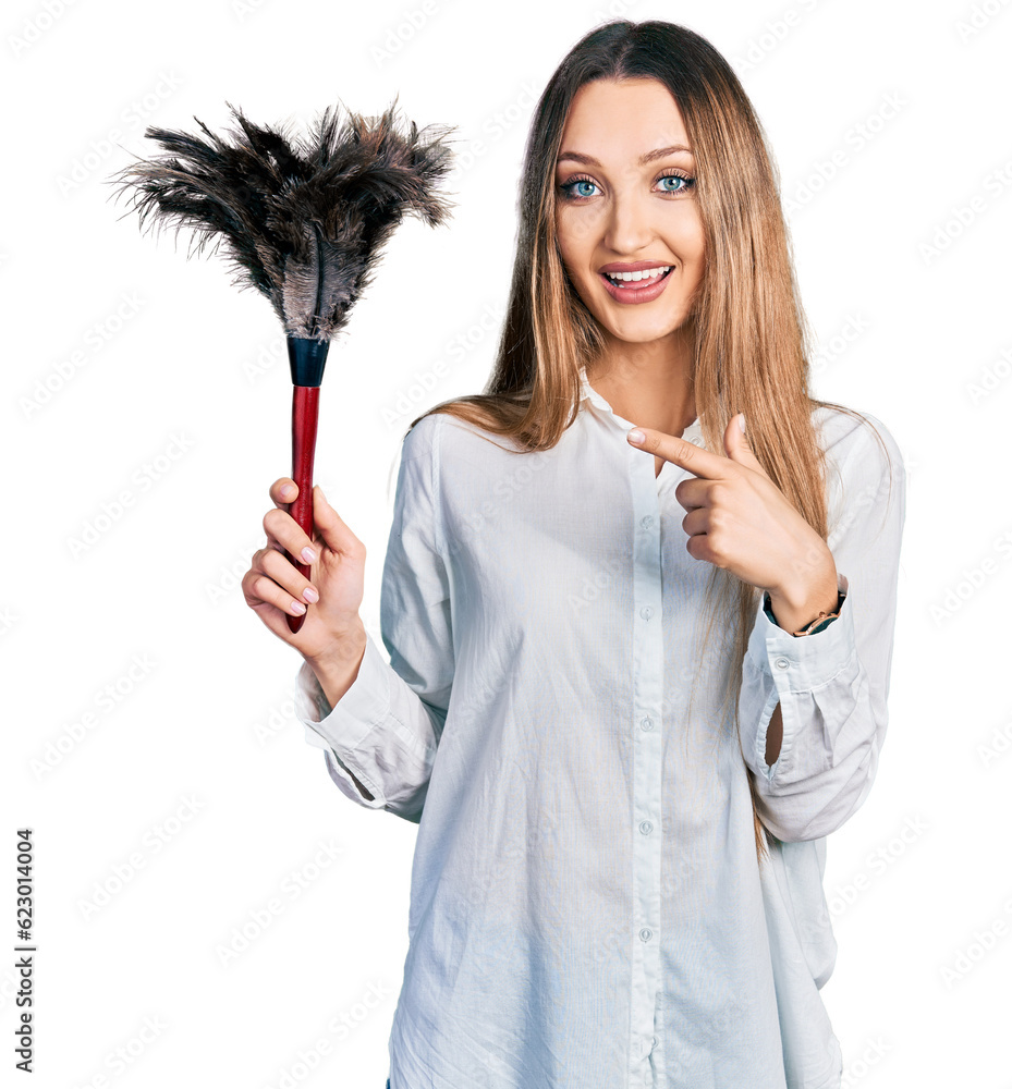 Beautiful caucasian woman holding cleaning duster smiling happy pointing with hand and finger Beautiful caucasian woman holding cleaning duster smiling happy pointing with hand and finger
