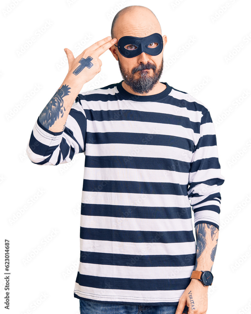 Young handsome man wearing burglar mask shooting and killing oneself pointing hand and fingers to head like gun, suicide gesture. Young handsome man wearing burglar mask shooting and killing oneself pointing hand and fingers to head like gun, suicide gesture.