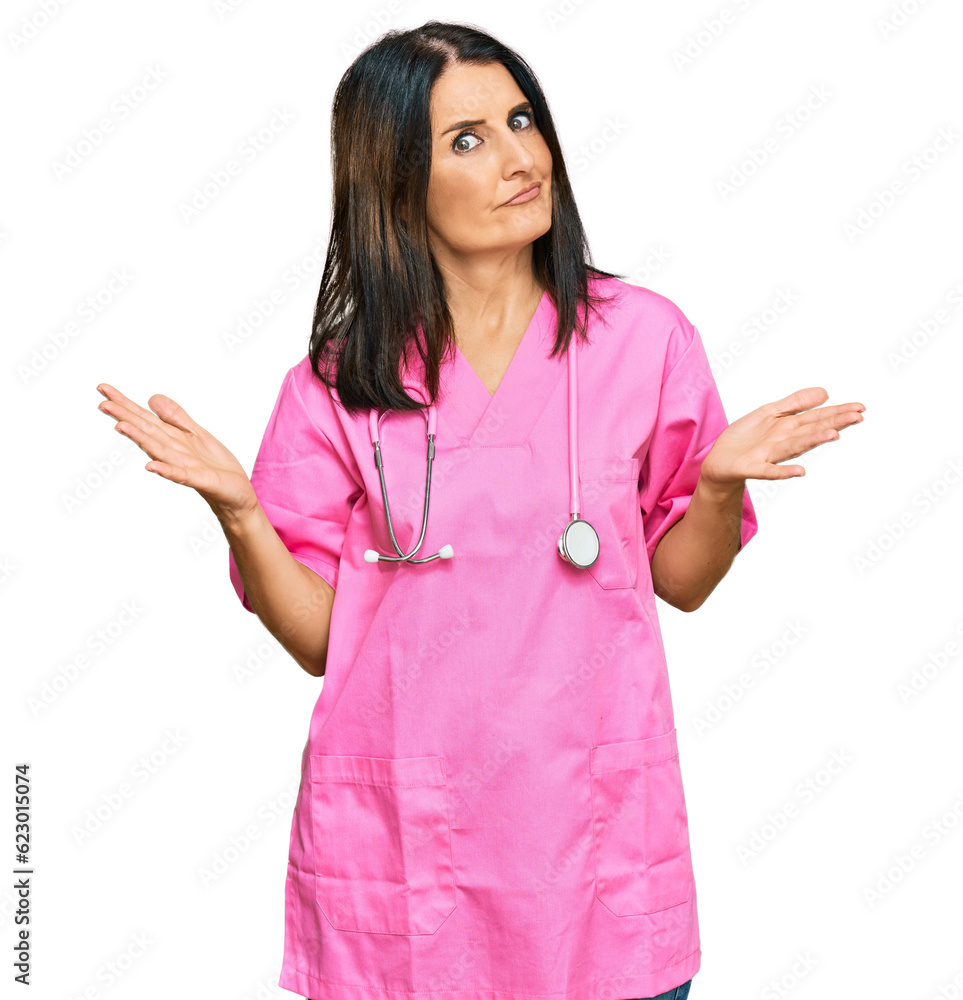 Middle age brunette woman wearing doctor uniform and stethoscope clueless and confused expression with arms and hands raised. doubt concept. Middle age brunette woman wearing doctor uniform and stethoscope clueless and confused expression with arms and hands raised. doubt concept.