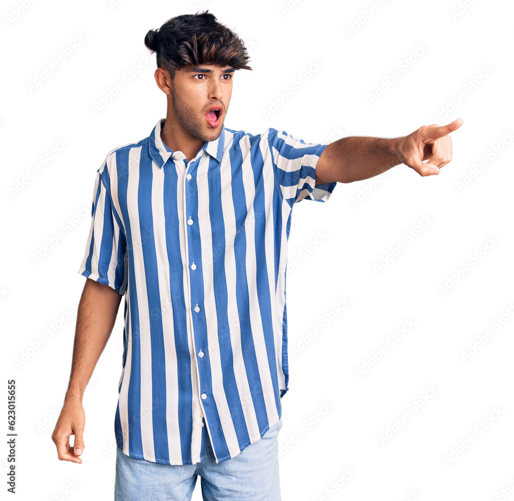 Young hispanic man wearing casual clothes pointing with finger surprised ahead, open mouth amazed expression, something on the front Young hispanic man wearing casual clothes pointing with finger surprised ahead, open mouth amazed expression, something on the front