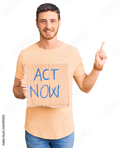 Handsome young man with bear holding act now banner surprised with an idea or question pointing finger with happy face, number one