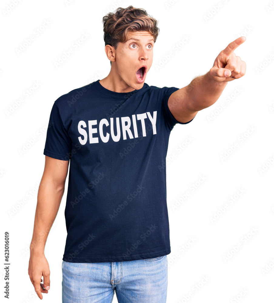 Young handsome man wearing security t shirt pointing with finger surprised ahead, open mouth amazed expression, something on the front Young handsome man wearing security t shirt pointing with finger surprised ahead, open mouth amazed expression, something on the front