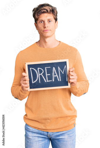 Young handsome man holding blackboard with dream word thinking attitude and sober expression looking self confident