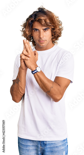 Young hispanic man wearing casual white tshirt holding symbolic gun with hand gesture  playing killing shooting weapons  angry face