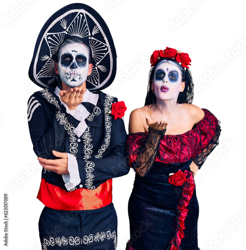 Young couple wearing mexican day of the dead costume over background looking at the camera blowing a kiss with hand on air being lovely and sexy. love expression.