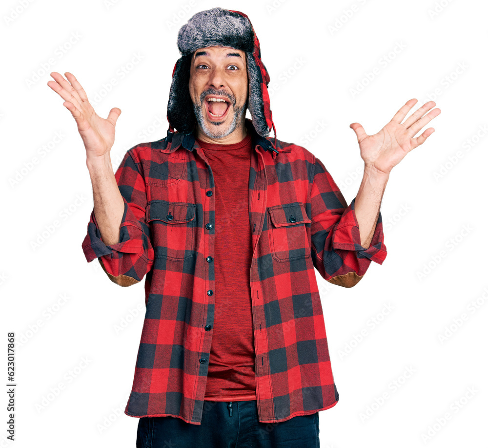 Middle age hispanic man with grey hair wearing fluffy earmuff hat celebrating crazy and amazed for success with arms raised and open eyes screaming excited. winner concept Middle age hispanic man with grey hair wearing fluffy earmuff hat celebrating crazy and amazed for success with arms raised and open eyes screaming excited. winner concept