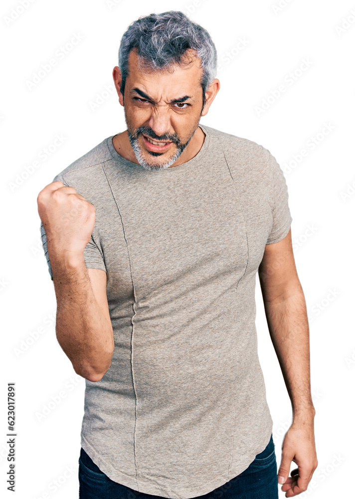 Middle age hispanic with grey hair wearing casual grey t shirt angry and mad raising fist frustrated and furious while shouting with anger. rage and aggressive concept. Middle age hispanic with grey hair wearing casual grey t shirt angry and mad raising fist frustrated and furious while shouting with anger. rage and aggressive concept.