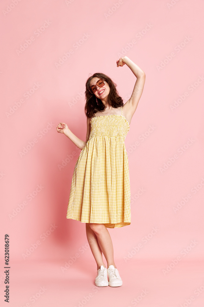 Full-length portrait of beautiful young woman in pretty yellow dress and sunglasses cheerfully dancing on pink studio background. Concept of human emotions, fashion, beauty, lifestyle, summer vibe, ad Full-length portrait of beautiful young woman in pretty yellow dress and sunglasses cheerfully dancing on pink studio background. Concept of human emotions, fashion, beauty, lifestyle, summer vibe, ad