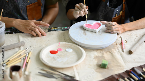 Two young creative man painting, decorating handmade dishes in workshop. Handicraft, creativity and hobby concept