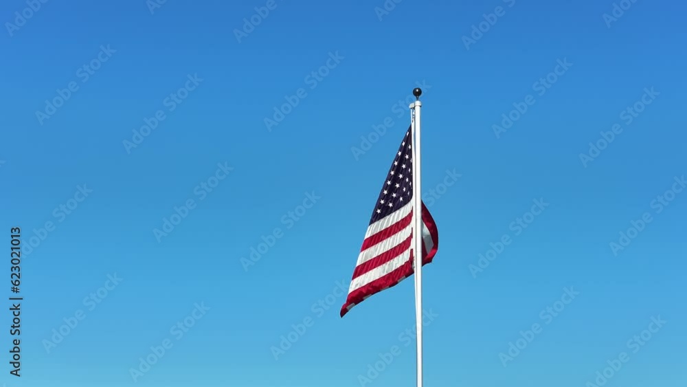American Flag on a pole waving flapping in the wind with no clouds and blue sky. American Flag on a pole waving flapping in the wind with no clouds and blue sky.