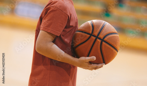 A basketball player holding a ball during a training session. Youth basketball team on practice unit. Basketball training session for school kids. College boys improving basketball skills © matimix