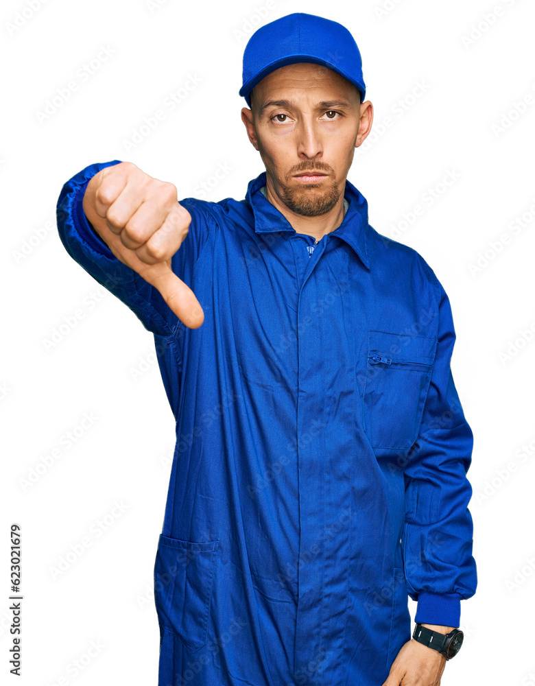 Bald man with beard wearing builder jumpsuit uniform looking unhappy and angry showing rejection and negative with thumbs down gesture. bad expression.