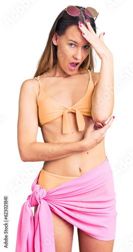 Beautiful brunette young woman wearing bikini and sunglasses surprised with hand on head for mistake, remember error. forgot, bad memory concept.