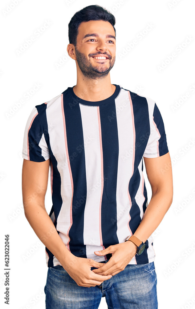 Young handsome hispanic man wearing striped tshirt looking away to side with smile on face, natural expression. laughing confident. Young handsome hispanic man wearing striped tshirt looking away to side with smile on face, natural expression. laughing confident.