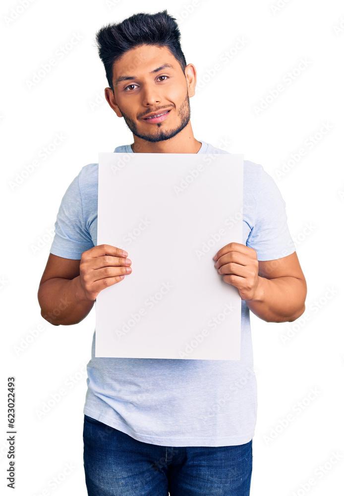 Handsome latin american young man holding cardboard banner with blank space looking positive and happy standing and smiling with a confident smile showing teeth Handsome latin american young man holding cardboard banner with blank space looking positive and happy standing and smiling with a confident smile showing teeth