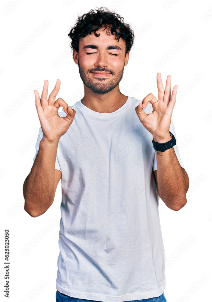 Hispanic young man with beard wearing casual white t shirt relaxed and smiling with eyes closed doing meditation gesture with fingers. yoga concept. Hispanic young man with beard wearing casual white t shirt relaxed and smiling with eyes closed doing meditation gesture with fingers. yoga concept.