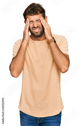 Handsome young man with beard wearing casual tshirt with hand on head, headache because stress. suffering migraine.